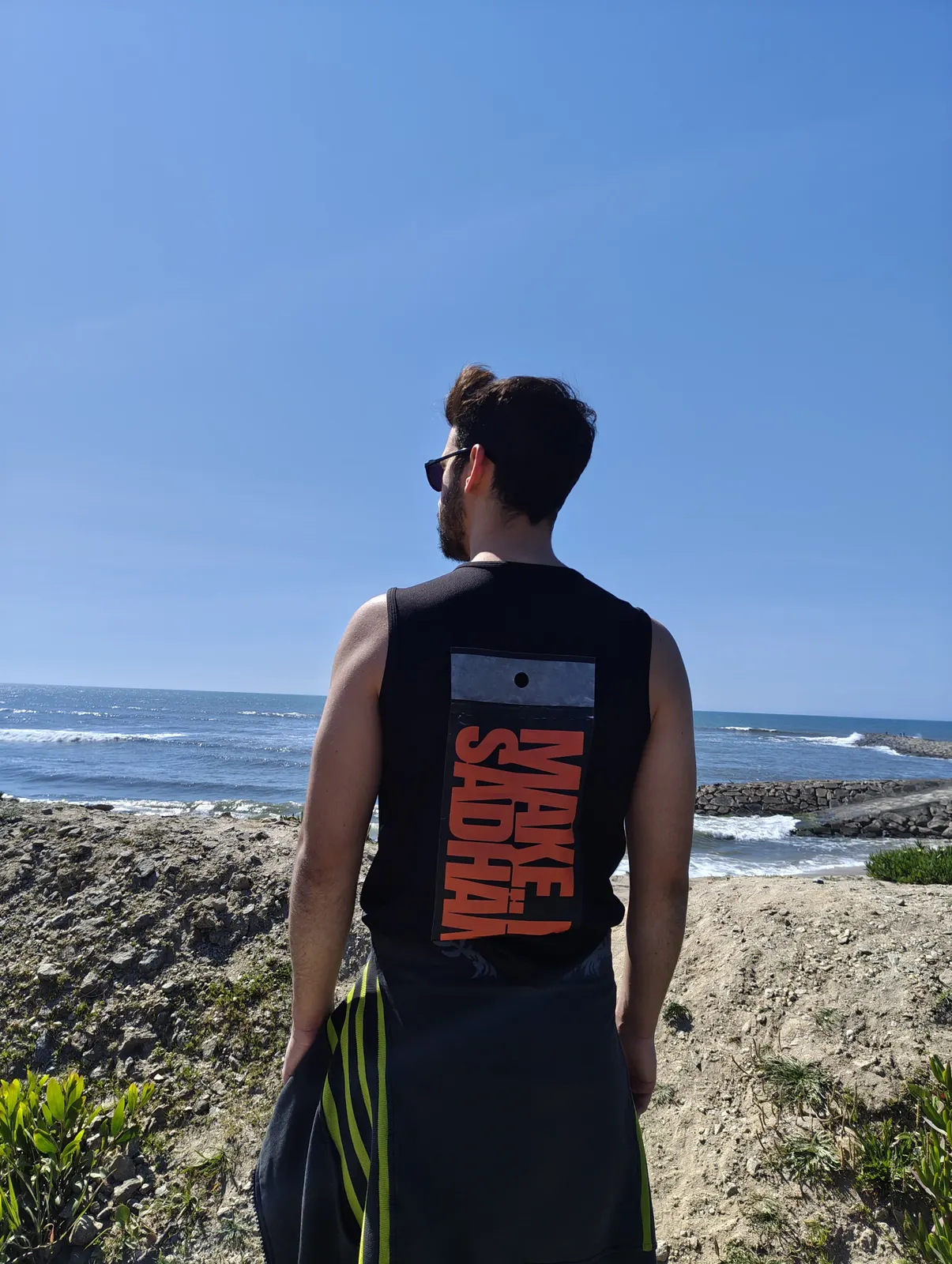 Sadhäna band member in a “Make Sadhäna” tank top overlooking the ocean