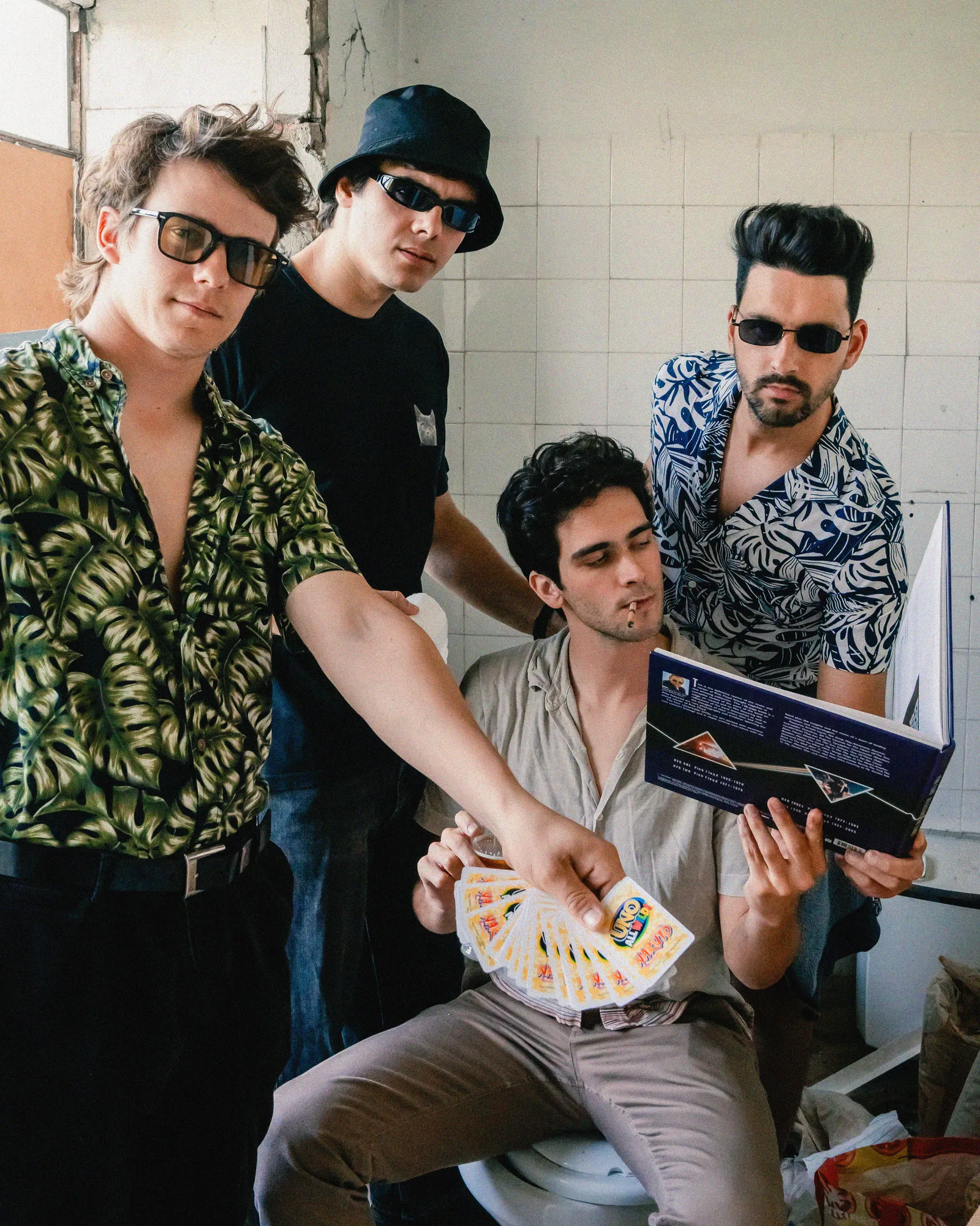 The four members of Sadhäna posing in a tiled room, one holding out a fan of playing cards